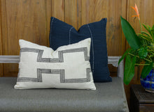 Load image into Gallery viewer, Mood shot of a hand blocked cotton lumbar cushion cover in a charcoal colour on an ivory cotton fabric, placed in  front of a hand woven navy cushion cover on a bench