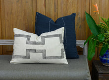 Load image into Gallery viewer, Mood shot of a hand blocked cotton lumbar cushion cover in a charcoal colour on an ivory cotton fabric, placed in  front of a hand woven navy cushion cover on a bench
