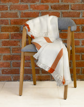 Load image into Gallery viewer, Hand woven woollen throw blanket in a terracotta and ivory colour placed on a chair against a brick wall.
