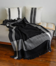 Load image into Gallery viewer, Hand woven woollen throw blanket in a black and ivory colour placed next to two block printed cushion covers on a day bed.
